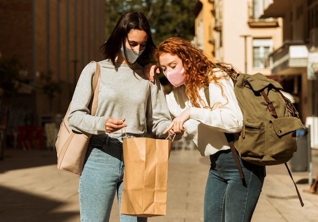 Foto gratuita vista frontal de amigas con mascarillas al aire libre con bolsa de compras