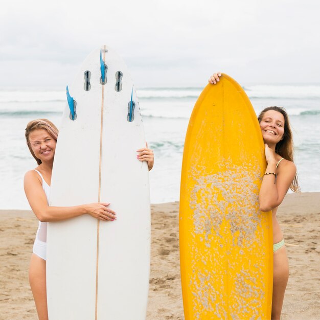 Vista frontal de amigas en la playa posando con tablas de surf