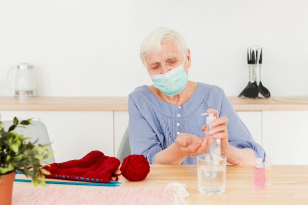 Foto gratuita vista frontal de una anciana con desinfectante para manos mientras teje