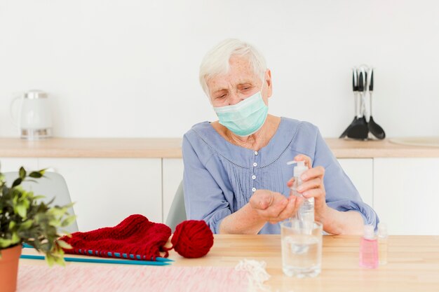 Vista frontal de una anciana con desinfectante para manos mientras teje