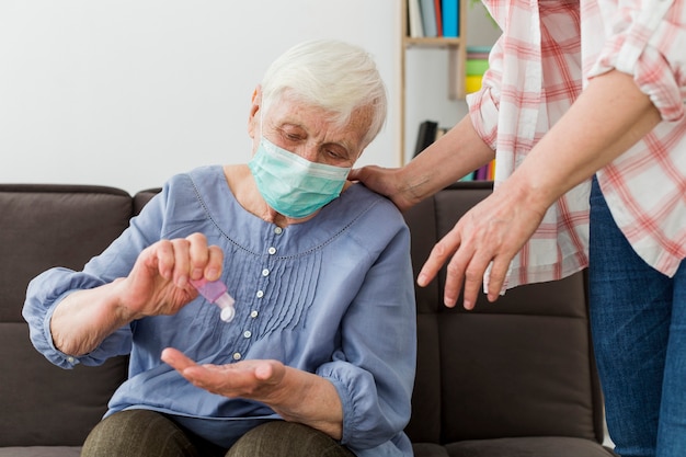 Vista frontal de una anciana con desinfectante para manos mientras usa una máscara médica