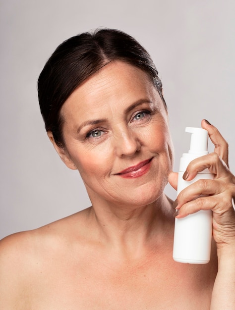Vista frontal de la anciana sonriente sosteniendo una botella de limpiador para el cuidado de la piel