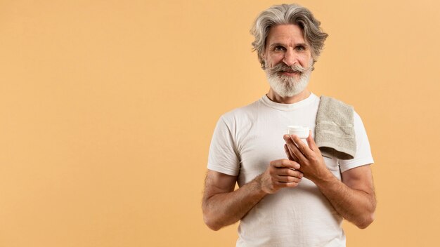 Vista frontal del anciano hombre barbudo que sostiene la crema hidratante con copia espacio