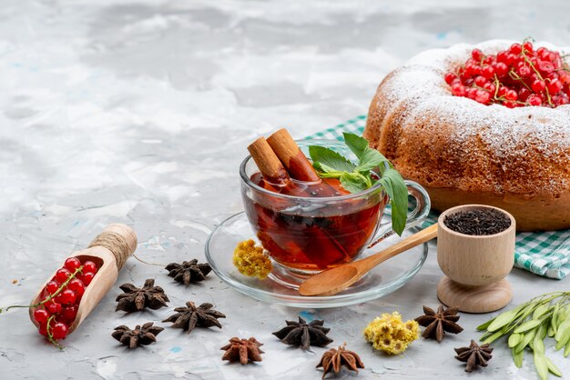 Una vista frontal de arándanos rojos frescos agrios y suaves con té de pastel redondo y canela en el escritorio blanco frutas bayas