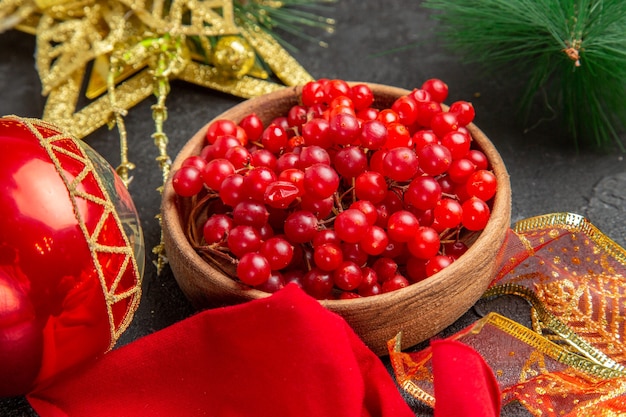 Vista frontal de arándanos rojos frescos alrededor de juguetes de navidad en color de fondo oscuro baya de frutas de vacaciones de navidad