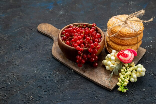 Vista frontal de arándanos rojos frescos dentro del recipiente con relleno de crema, galletas sándwich en la superficie oscura dulce de azúcar