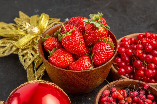 Vista frontal de arándanos rojos frescos con otras frutas alrededor de juguetes de navidad en el color de fondo oscuro baya de frutas de vacaciones de navidad