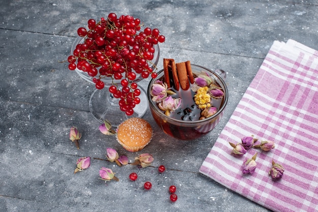 Vista frontal de arándanos rojos frescos con una taza de té y canela en la mesa de luz, té fresco de frutas y bayas