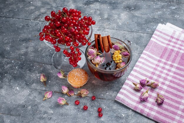 Vista frontal de arándanos rojos frescos con una taza de té y canela en la mesa de luz, té fresco de frutas y bayas