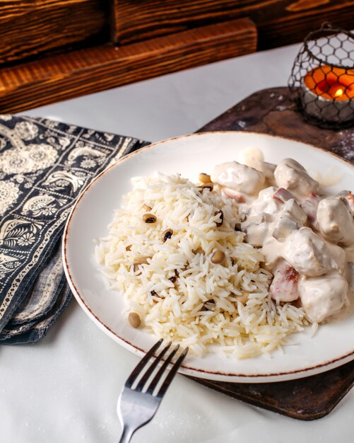 Vista frontal de arroz cocido junto con frijoles y rodajas de carne dentro de un plato blanco sobre la superficie de madera