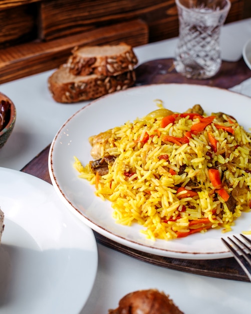 Vista frontal de arroz cocido con verduras frescas en rodajas dentro de un plato blanco en el piso blanco