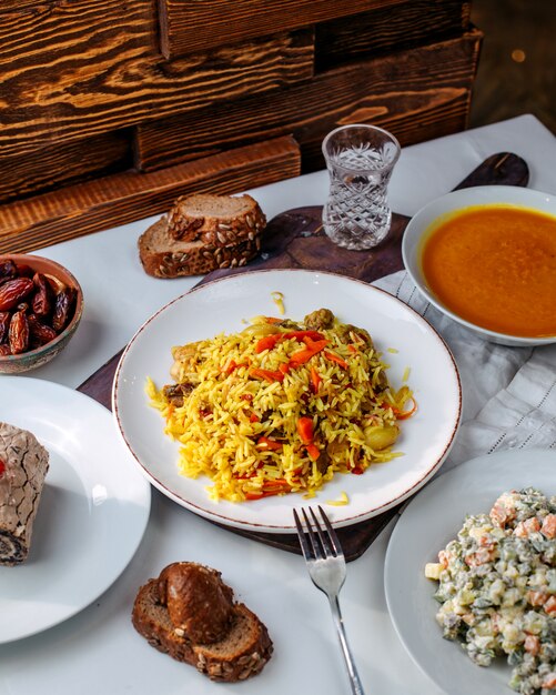 Vista frontal de arroz cocido con verduras fritas junto con panecillos de ensalada y sopa en el piso blanco