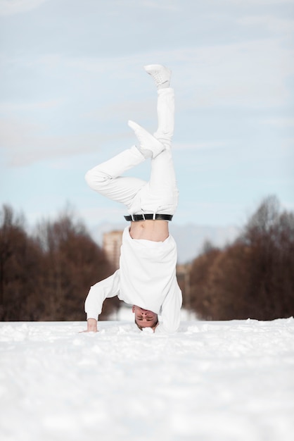 Vista frontal del artista masculino de hip hop de pie sobre la cabeza en la nieve.