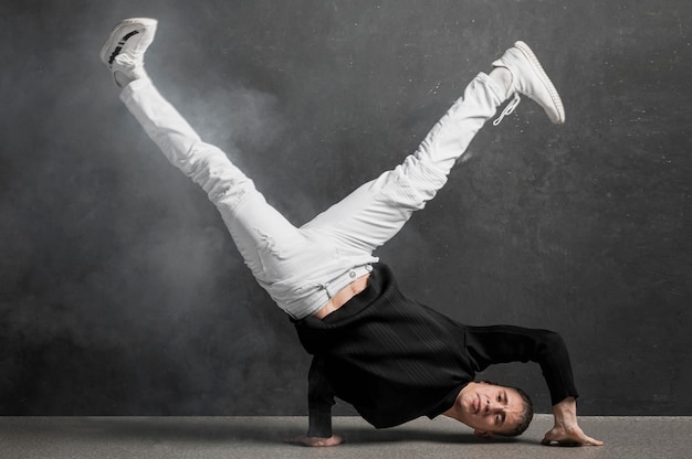 Vista frontal del artista masculino en jeans y zapatillas posando mientras sostiene las piernas