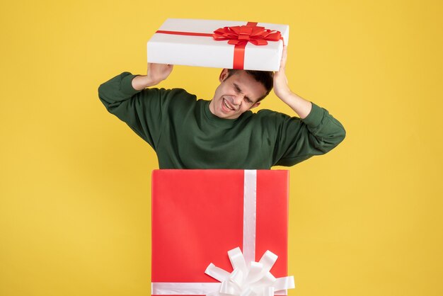 Vista frontal asustado joven parado detrás de caja de regalo grande en amarillo