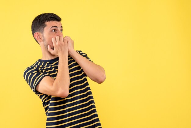 Vista frontal asustado macho joven en blanco y negro camiseta a rayas fondo amarillo aislado