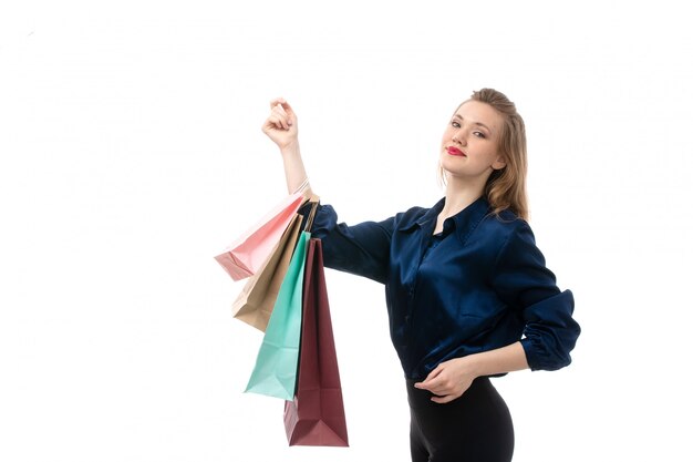 Una vista frontal atractiva joven en blusa azul pantalón negro posando sosteniendo paquetes de compras en el fondo blanco, ropa elegante de moda