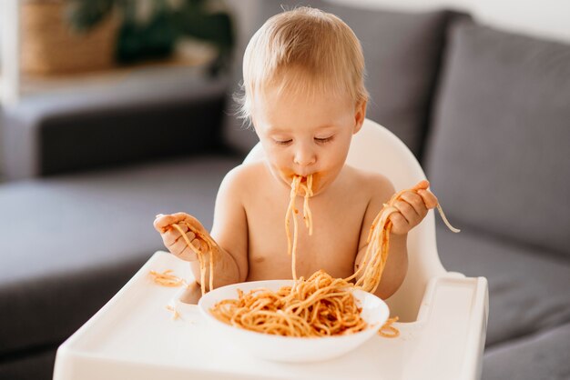 Vista frontal Baby Boy jugando con pasta en su trona