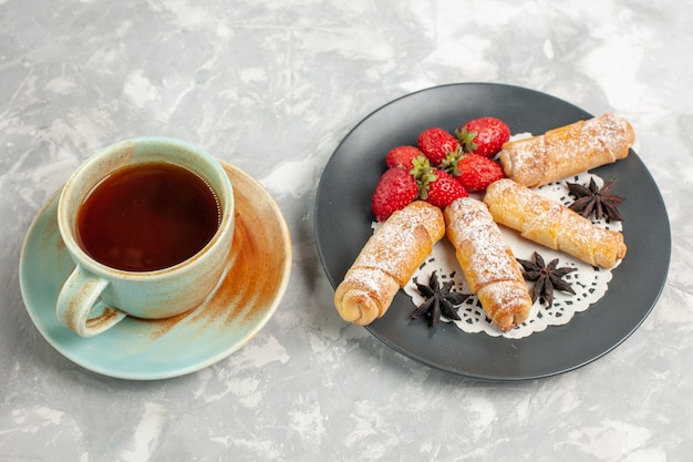 Vista frontal de bagels de azúcar en polvo con fresas y taza de té