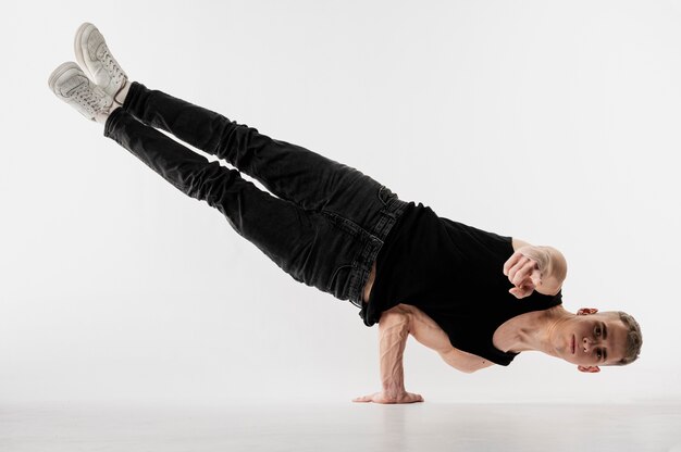 Vista frontal del bailarín masculino en jeans y zapatillas posando mientras levanta su cuerpo en un brazo