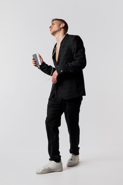 Vista frontal del bailarín en traje y zapatillas con smartphone y auriculares
