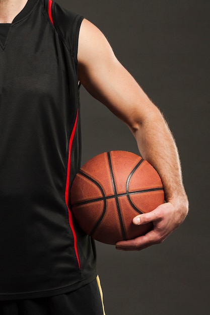 Foto gratuita vista frontal del baloncesto sostenido por el jugador cerca del cuerpo