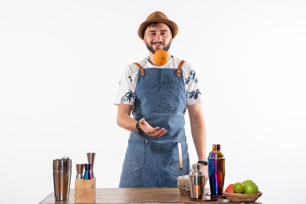 Vista frontal del barman masculino frente al escritorio de la barra jugando con frutas en el piso blanco bar alcohol trabajo nocturno club de bebidas de frutas