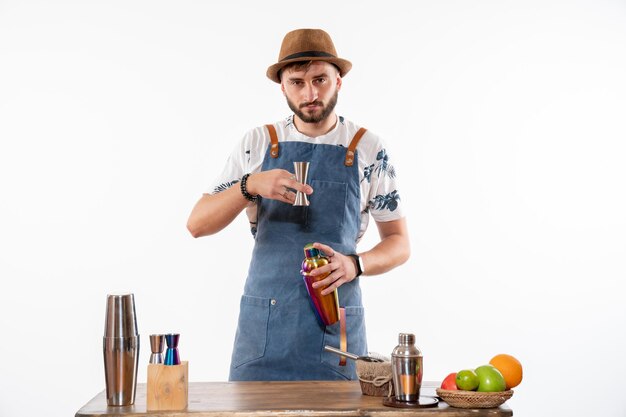 Vista frontal del barman masculino frente a la mesa de la barra preparando una bebida en la coctelera en la pared blanca clara bar trabajo de alcohol bebida de frutas club de noche