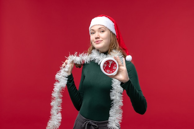 Vista frontal bastante mujer sosteniendo el reloj en un piso rojo rojo año nuevo vacaciones navidad