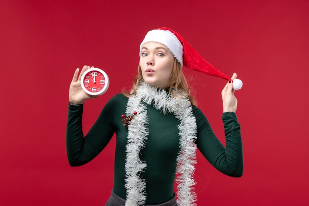 Vista frontal bastante mujer sosteniendo el reloj sobre el fondo rojo.