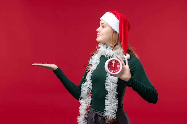 Foto gratuita vista frontal bastante mujer sosteniendo el reloj sobre el fondo rojo.