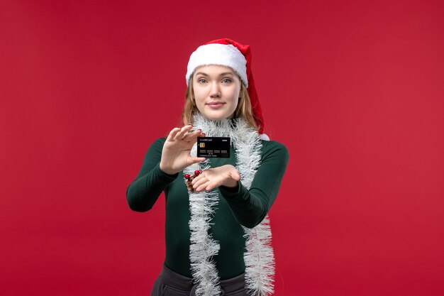 Vista frontal bastante mujer sosteniendo una tarjeta bancaria negra sobre fondo rojo.