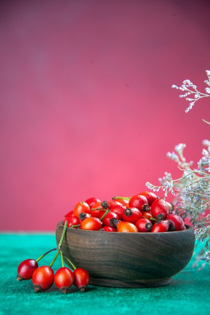 Vista frontal de las bayas rojas dentro de la placa en el escritorio verde-rosa berry frutos silvestres color de salud