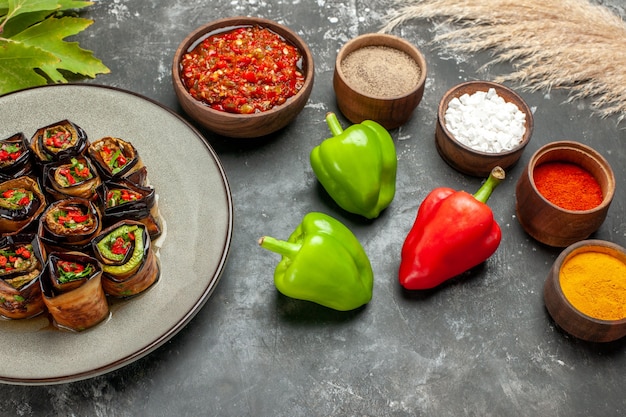 Vista frontal de berenjena rellena rollos de especias en tazones pequeños sal pimienta pimiento rojo cúrcuma pimientos adjika en gris