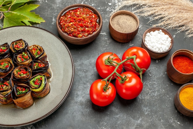 Vista frontal de berenjena rellena rollos de especias en tazones pequeños sal pimienta pimiento rojo cúrcuma tomates adjika sobre fondo gris