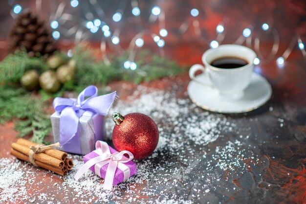 Vista frontal bola de árbol de Navidad pequeños regalos taza de té en polvo de coco sobre fondo oscuro aislado