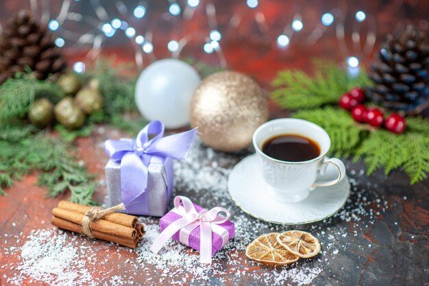 Vista frontal bolas de árbol de Navidad taza de té pequeños regalos polvo de coco sobre fondo oscuro aislado