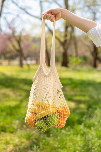 Foto gratuita vista frontal bolsa reutilizable en mano de mujer en la naturaleza