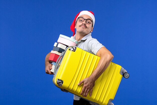 Vista frontal de la bolsa de transporte de hombres jóvenes y regalos en el avión de vacaciones de vuelo de escritorio azul