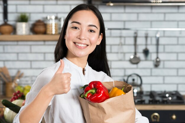 Vista frontal de la bolsa de verduras de la mujer mientras se muestra el pulgar