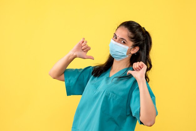 Foto gratuita vista frontal de la bonita doctora con máscara médica apuntando a sí misma en la pared amarilla