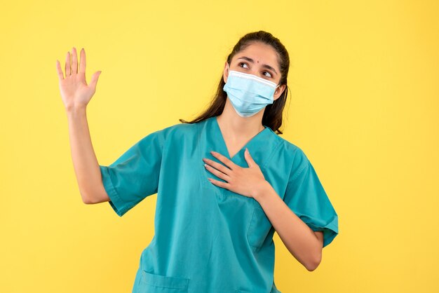 Vista frontal de la bonita doctora con máscara médica prometedora en la pared amarilla