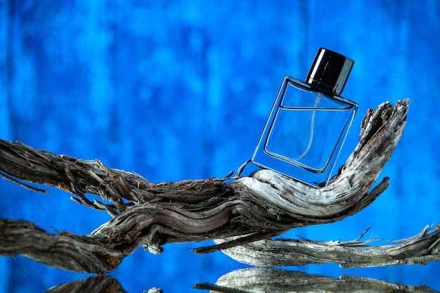 Vista frontal de la botella de colonia de los hombres en la rama de un árbol podrido aislado sobre fondo azul.