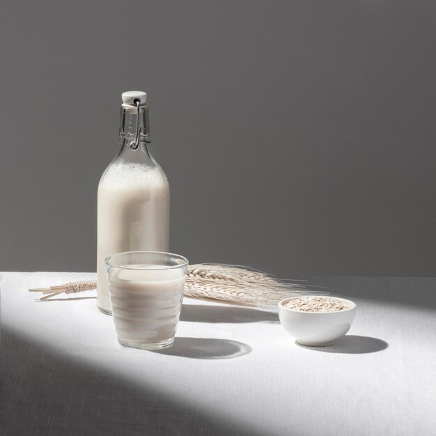 Vista frontal de la botella de leche con vaso lleno y tazón de avena