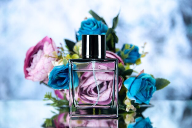 Vista frontal de la botella de perfume de rectángulo flores de colores sobre fondo azul claro borroso