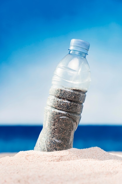 Foto gratuita vista frontal de la botella de plástico llena de arena en la playa