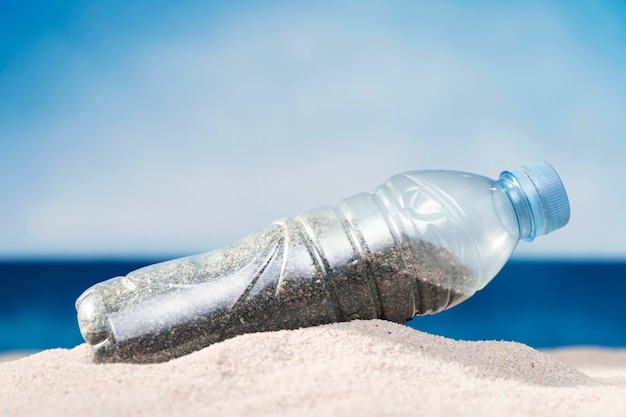 Vista frontal de la botella de plástico en la playa con arena