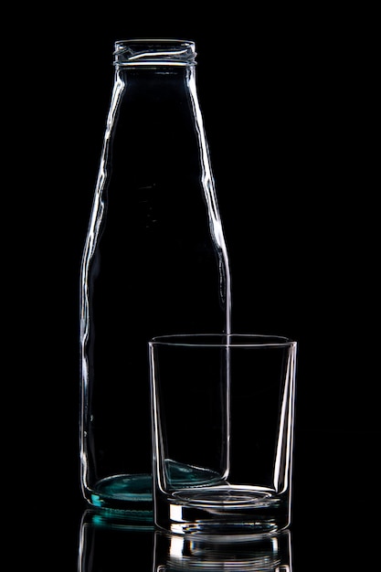 Vista frontal de la botella vacía y un vaso sobre fondo negro con espacio libre