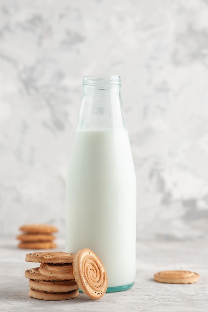 Vista frontal de una botella de vidrio abierta llena de leche y galletas sobre fondo blanco manchado con espacio libre