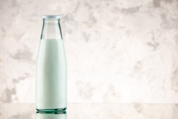Vista frontal de la botella de vidrio cerrada y llena con leche en el lado derecho sobre fondo de humo blanco con espacio libre